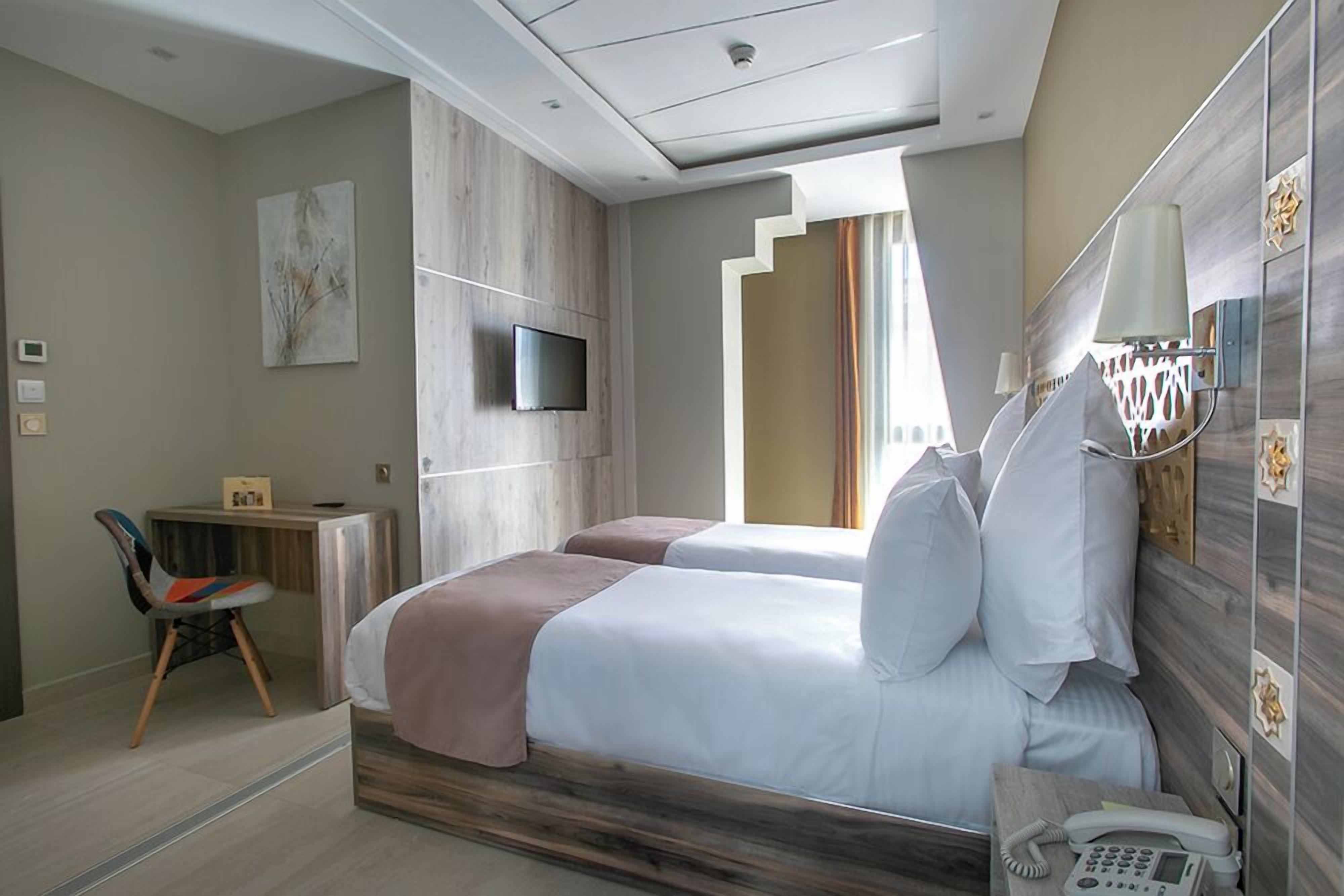 A hotel room with a bed, bedside table with a phone, a TV mounted on the wall, and a chair.