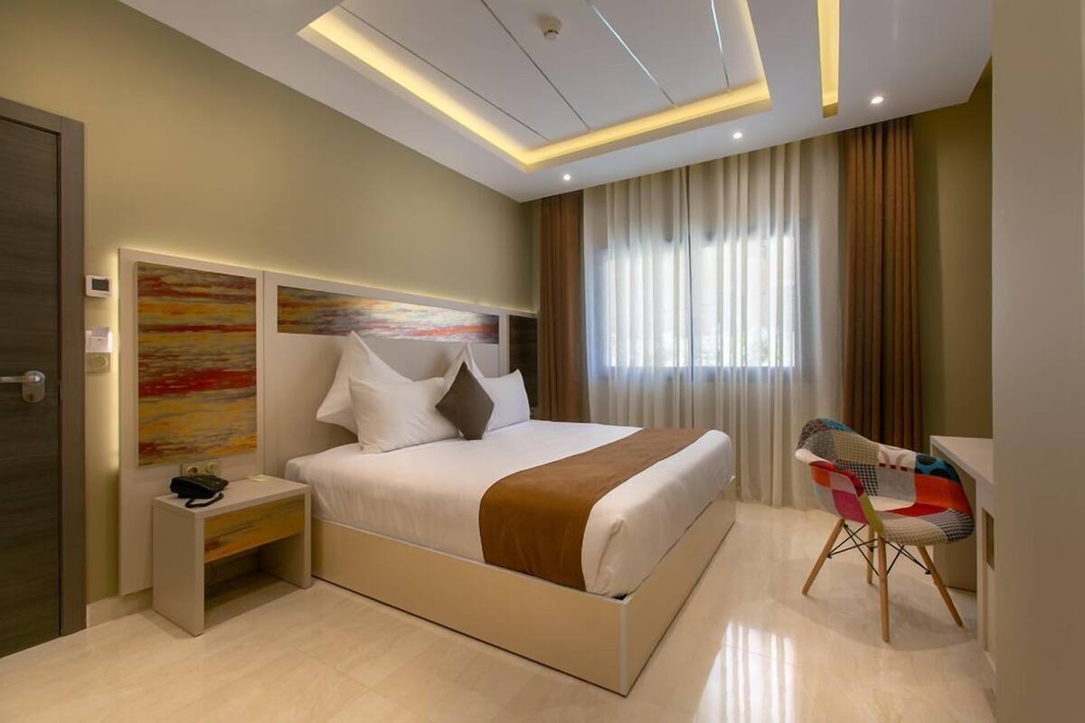 Una habitación de hotel moderna con una cama grande, mesitas de noche, un escritorio y una silla.