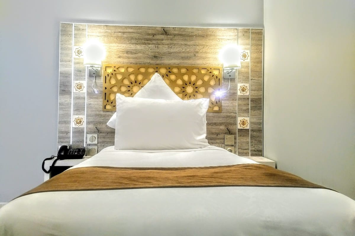 Una cama bien hecha con un cabecero de madera y dos lámparas de pared.