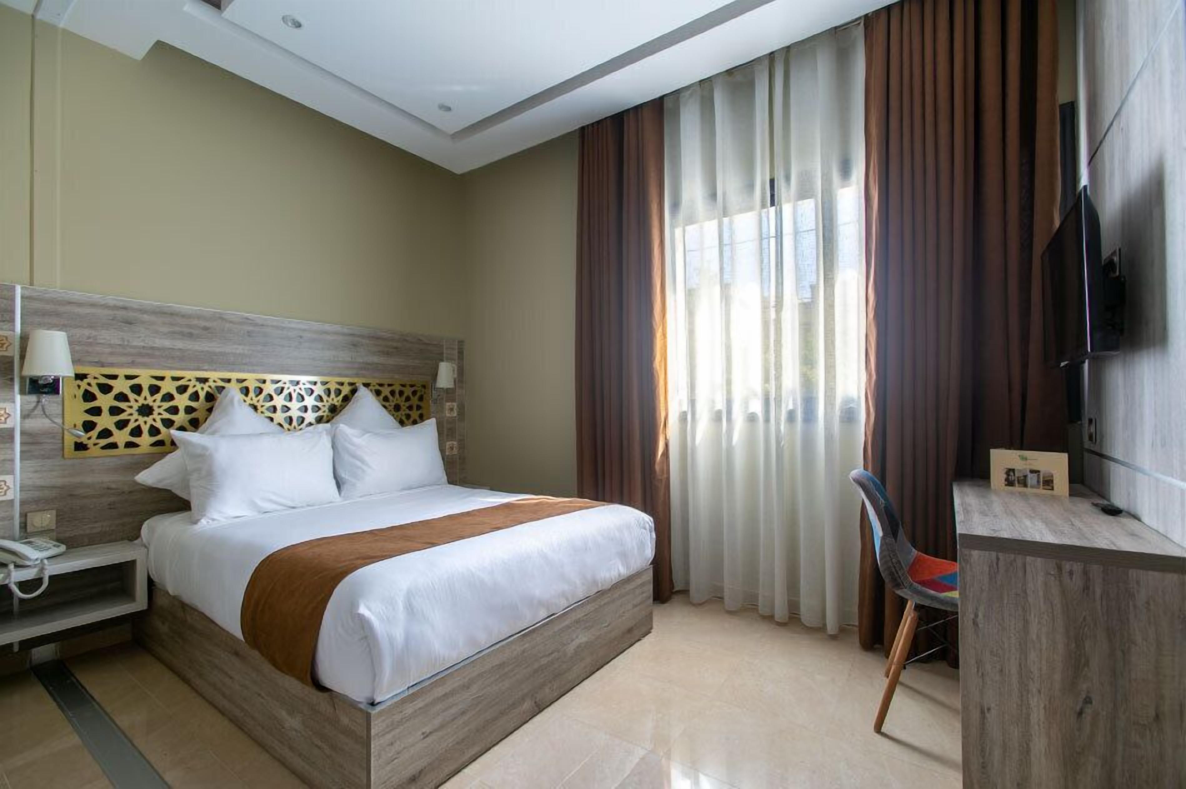 Una habitación de hotel con una cama de madera, un escritorio, una silla, un televisor y cortinas.