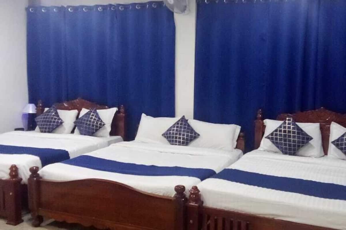 Una habitación de hotel con tres camas de madera, cada una con una colcha y almohadas a juego en blanco y azul.