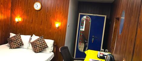 A hotel room with a bed, a desk, a chair, a clock, and a door.