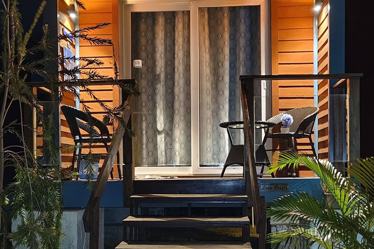 Una casa de madera con un porche, una escalera y dos sillas.