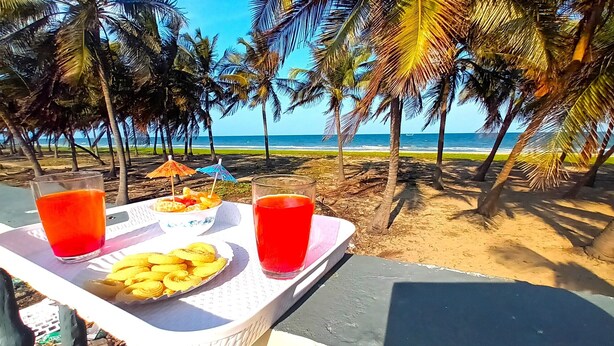 A beachside table with a tray containing a plate of pastries, two glasses of red beverage, and a bowl of fruit. - Chan Beach Resort (Bahur)