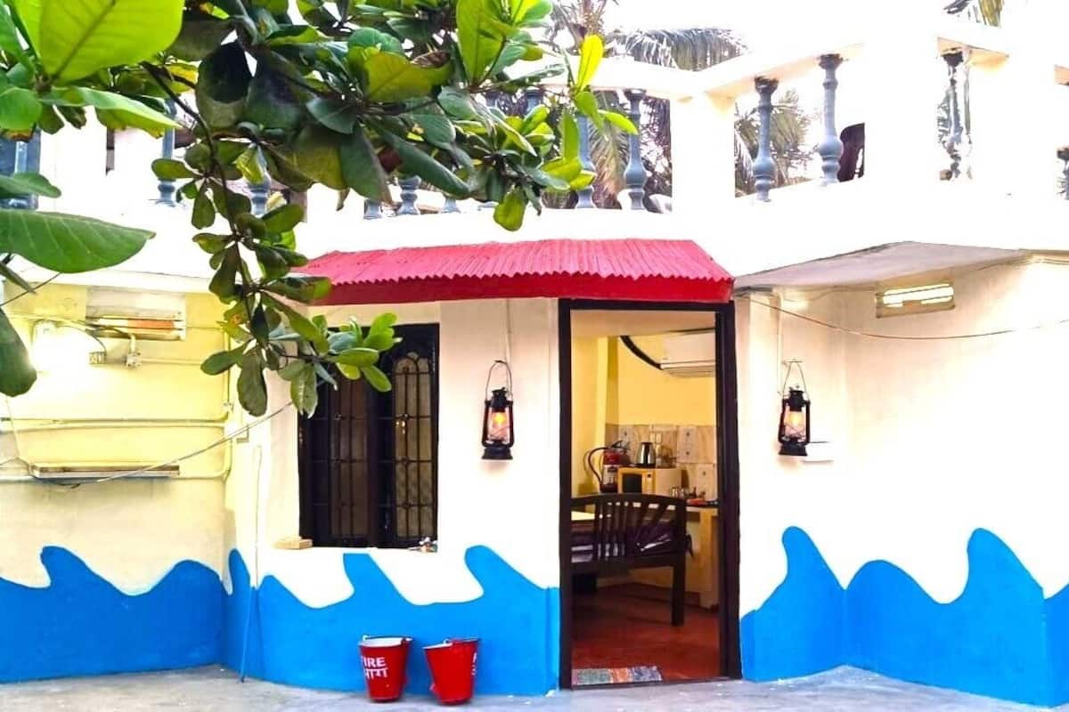 Un edificio de dos plantas con un toldo rojo sobre la entrada, se ve una cocina en el interior y un diseño de olas azules en las paredes exteriores.