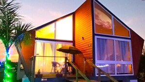 A modern house with a large glass window, a wooden deck, and a staircase leading to the entrance. - Chan Beach Resort (Bahur)