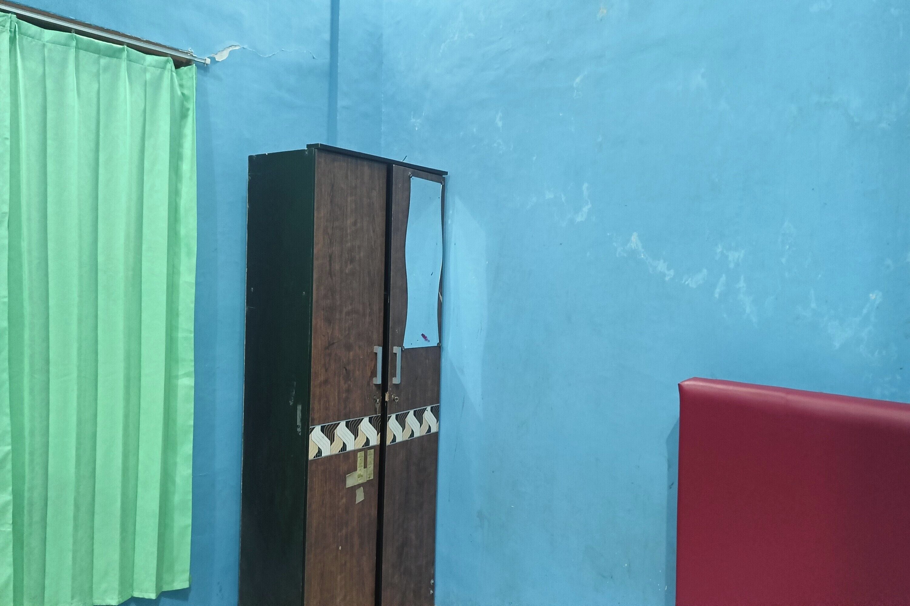 Una habitación con pared azul, cortina verde, armario de madera y sofá rojo.