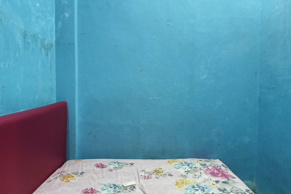 A corner of a room with a red upholstered headboard, a floral-patterned bedspread, and a blue wall.