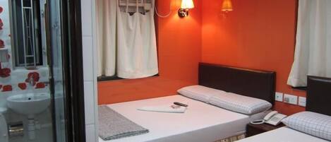 A hotel room with a bed, bedside table, lamp, and a bathroom with a shower and sink.