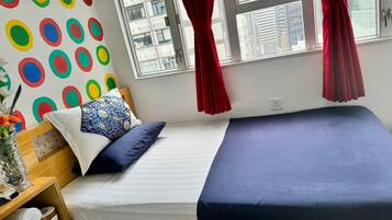 A neatly made bed with a blue and white bedspread, a wooden headboard, and a wall with colorful circular patterns.