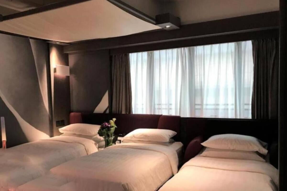 Hotellihuone, jossa on kaksi sänkyä, suuri ikkuna, jossa on verhot, ja moderni kattorakenne.