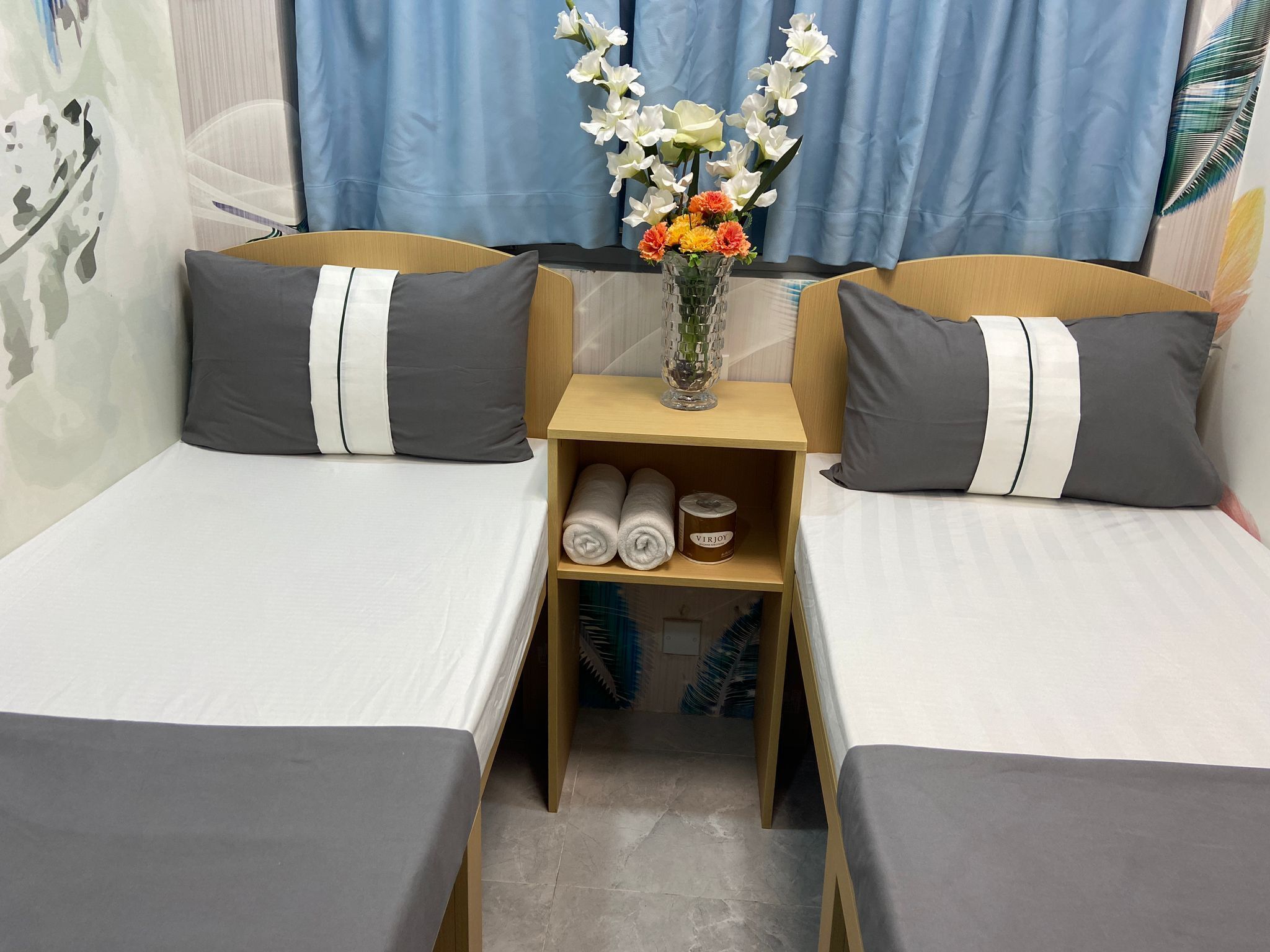 A small, neatly arranged room with two beds, a nightstand, and a vase of flowers.