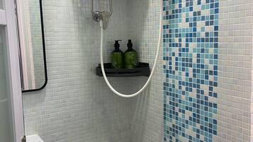 A small bathroom with a toilet, a shower, and a shelf with toiletries.