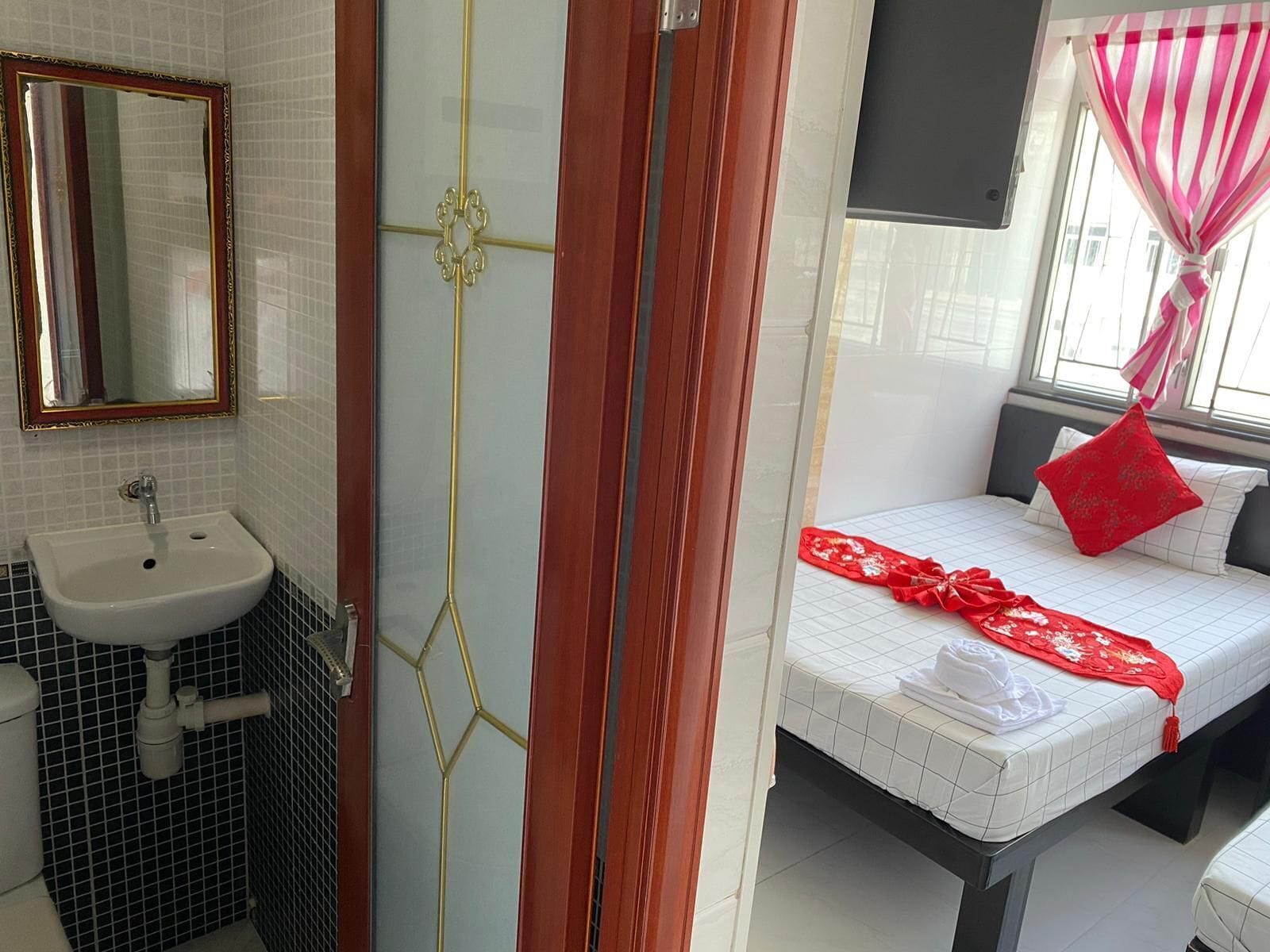 Une chambre d’hôtel avec une salle de bain, un lit recouvert d’une couverture rouge et une fenêtre avec des rideaux.