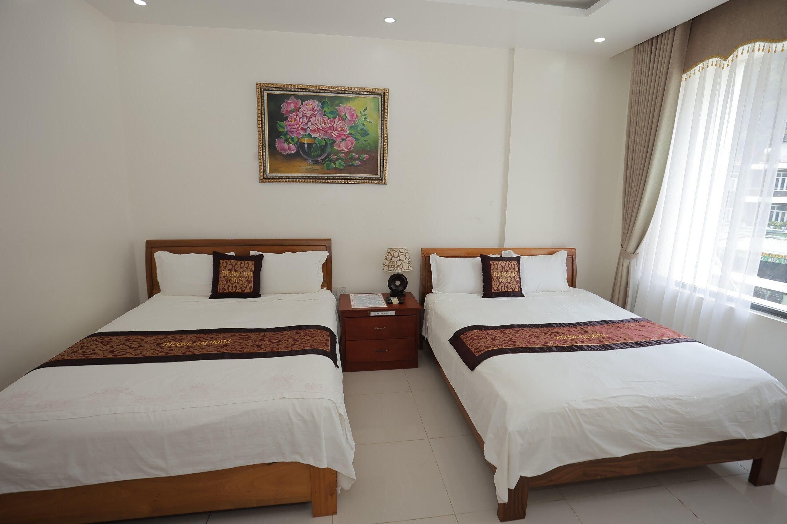 Habitación de hotel con dos camas, una mesita de noche, un cuadro en la pared y una ventana con cortinas.
