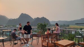 A terrace with outdoor seating, a view of mountains, and a clear sky. - Phong Nha Jasmine Hostel & Roof Top Bar (Phong Nha)