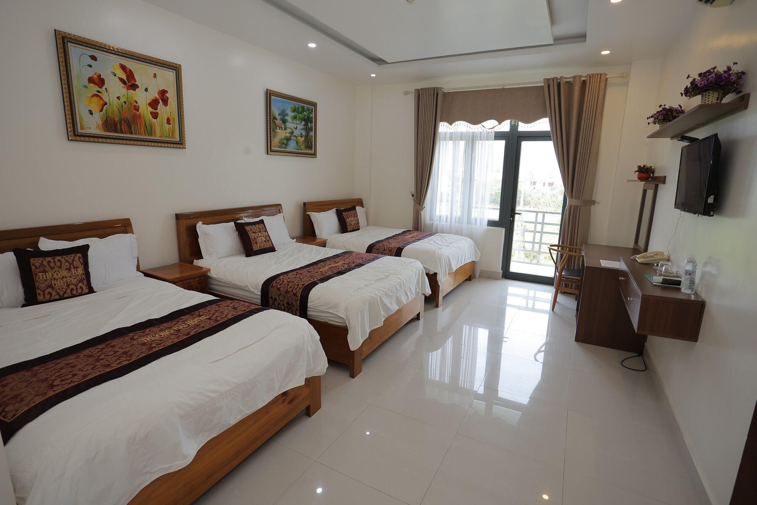 A hotel room with three beds, a desk, a TV, and a window with curtains.
