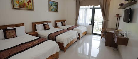 A hotel room with three beds, a desk, a TV, and a window with curtains.