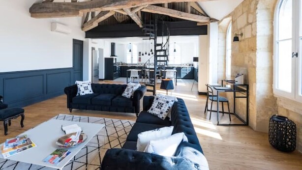 A spacious living area with dark sofas, a coffee table, and a staircase leading to an upper level. - Magnifique Loft Type Boutique Hôtel à Libourne (Libourne)