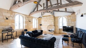 A spacious living room with exposed wooden beams, stone walls, and large windows. - Magnifique Loft Type Boutique Hôtel à Libourne (Libourne)