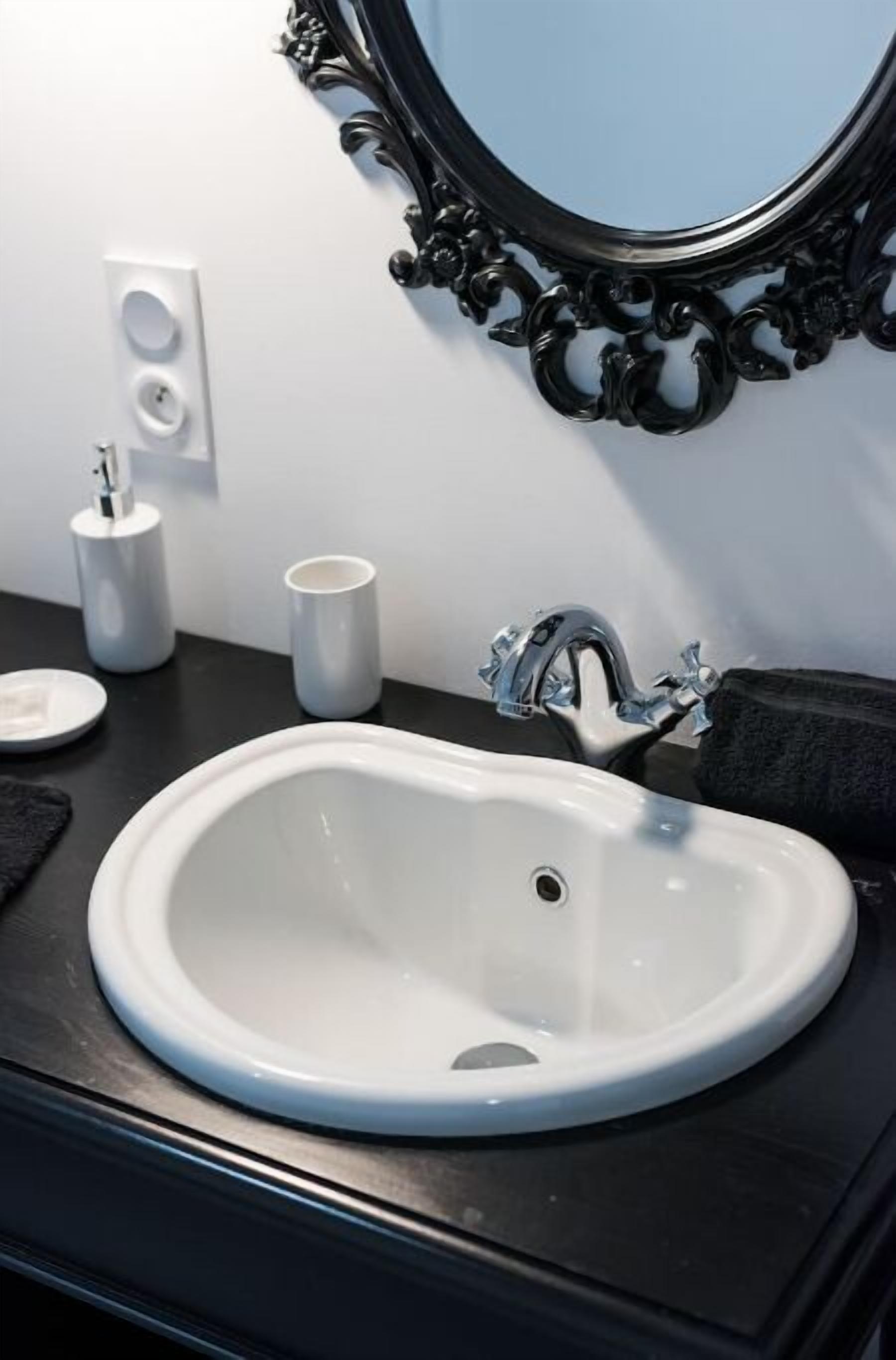 Une salle de bain avec un lavabo blanc, un plan de toilette noir et un grand miroir noir à motifs.