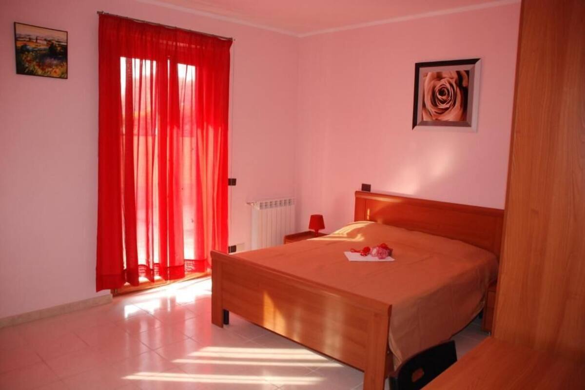 A bedroom with a wooden bed, red curtains, a radiator, and a framed picture on the wall.