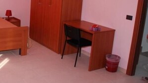 Un dormitorio con un armario de madera, un escritorio con silla y una mesita de noche con una lámpara roja.