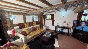 A cozy living room with exposed wooden beams, a sofa with patterned cushions, a coffee table, and a television.