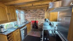 A compact kitchen with wooden cabinets, a brick wall, a built-in stove, and stainless steel appliances.