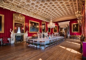 A grand dining room with a long table, ornate ceiling, and classical decor.