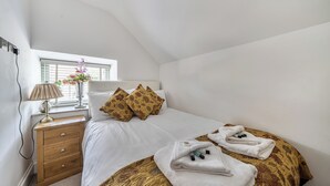 Une chambre à coucher avec un lit, des oreillers, une table de chevet, une lampe et une fenêtre.