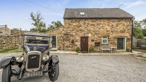 Une voiture ancienne est garée devant un bâtiment en pierre, avec une allée gravillonnée.