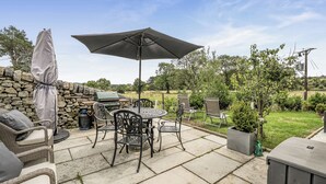 Une terrasse extérieure équipée d’un barbecue, de sièges et d’un grand parasol.