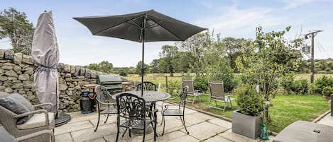 An outdoor patio with a grill, seating, and a large umbrella.