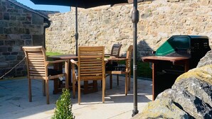 An outdoor patio with a stone wall, wooden chairs, a table, a grill, and an umbrella. - Barn-sleeps 4 Alton Towers Scarefest/peak District (Stoke-on-Trent)