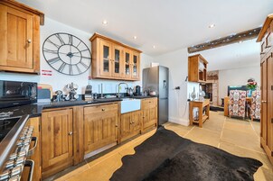 A kitchen with wooden cabinets, a large wall clock, a refrigerator, and a black rug.