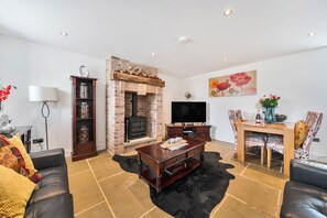 A living room with a fireplace, a television, a sofa, and a dining area with chairs. - Stylish Cosy Rustic Barn Alton Towers Peaks (Leek)