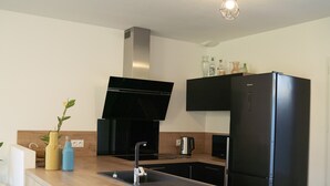 A modern kitchen with a black stove, a black refrigerator, and a wooden countertop. - Maison La Fontaine - Paisible & Verdoyante (Trélazé)