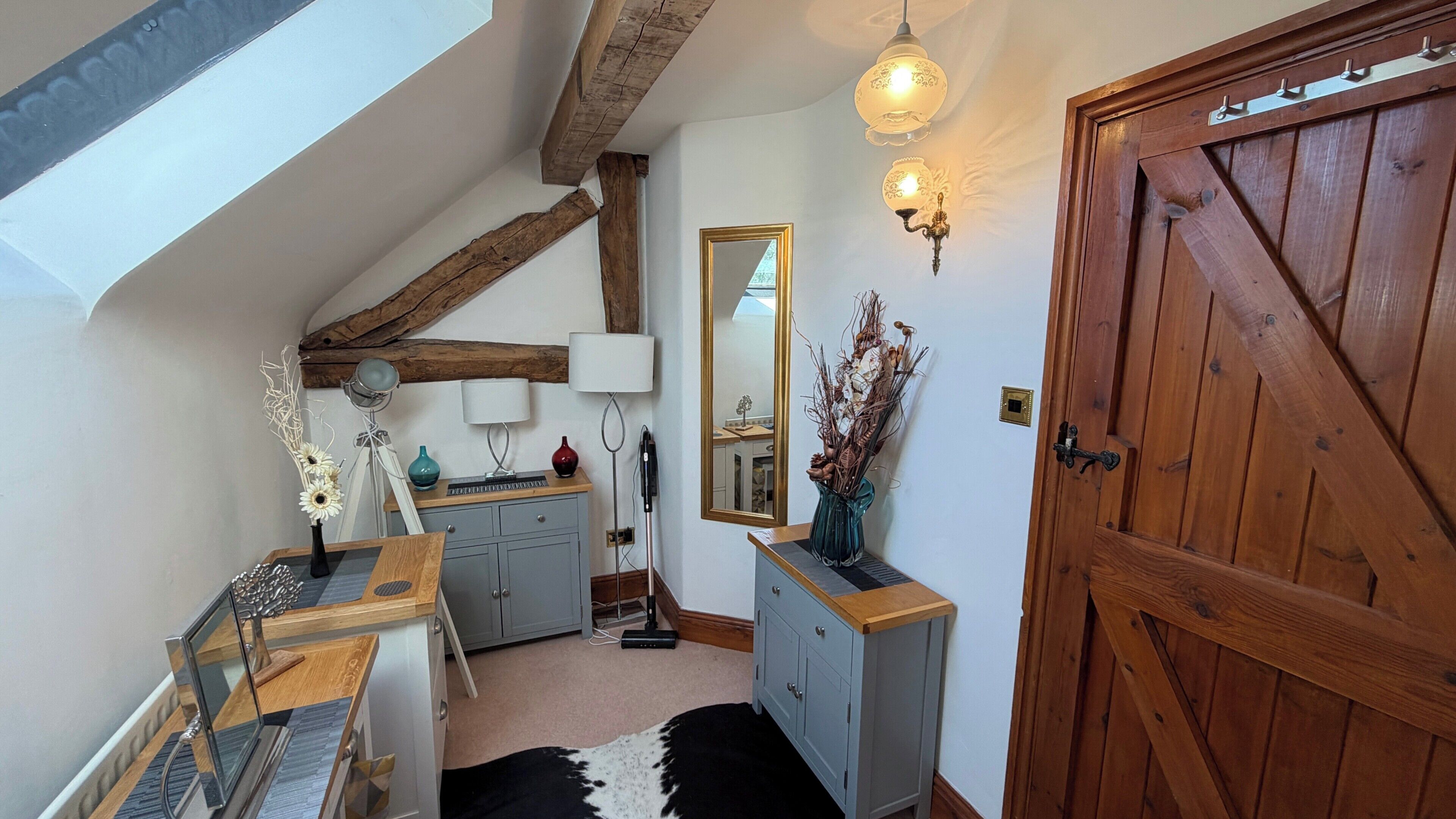 A room with a sloped ceiling, a wooden door, a mirror, and a cabinet with a vase.