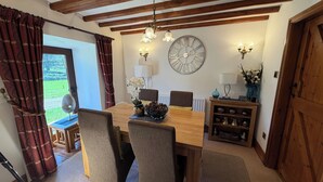Un comedor con mesa de madera, sillas, un reloj, apliques de pared y vistas al exterior.