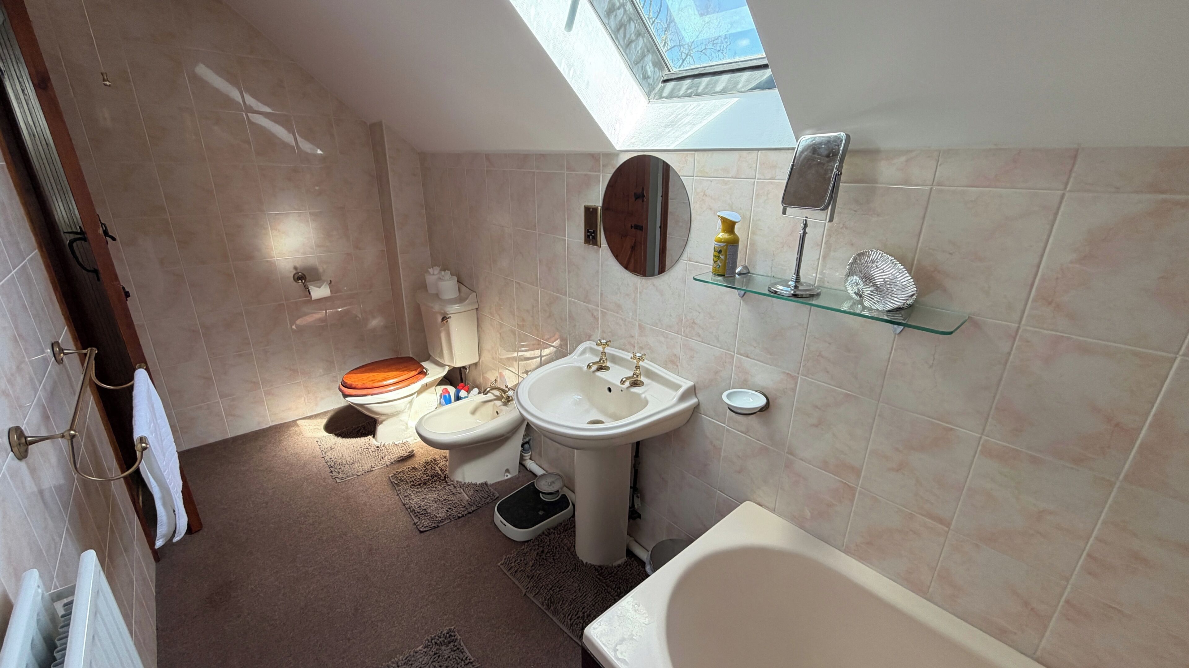 A bathroom with a skylight, a toilet, a bidet, a sink, and a bathtub.