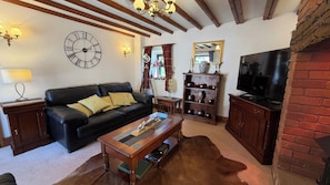 A living room with a black leather sofa, wooden coffee table, a clock on the wall, a television, and a fireplace. - Barn-sleeps 4-parking-near Alton Towers/peak Dist (Stoke-on-Trent)