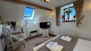 Una habitación de hotel con cama, televisor, ventilador, ventana con cortinas, radiador y toallero.
