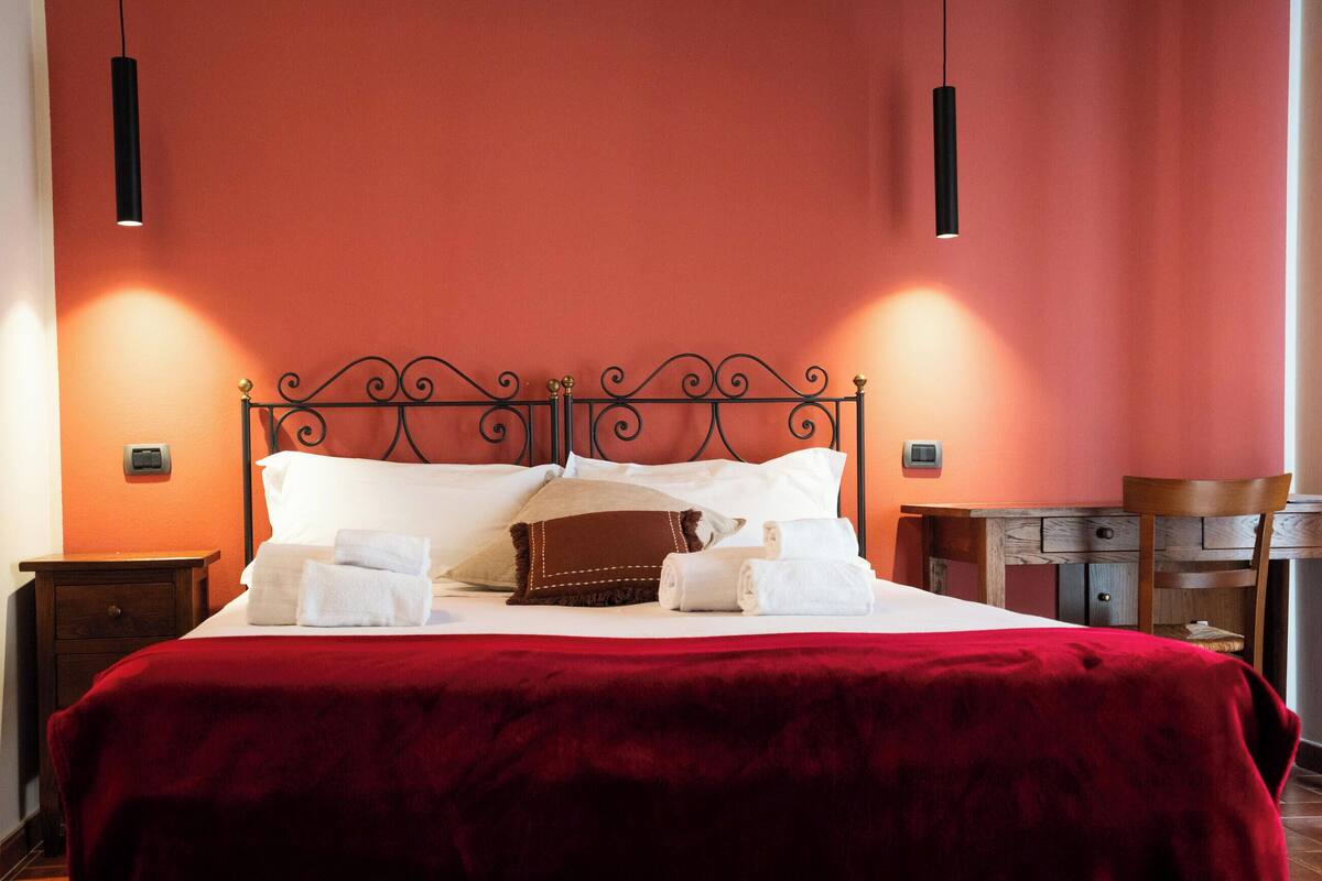 Una cama bien hecha con ropa de cama blanca y marrón, una manta roja y dos mesitas de noche con lámparas.