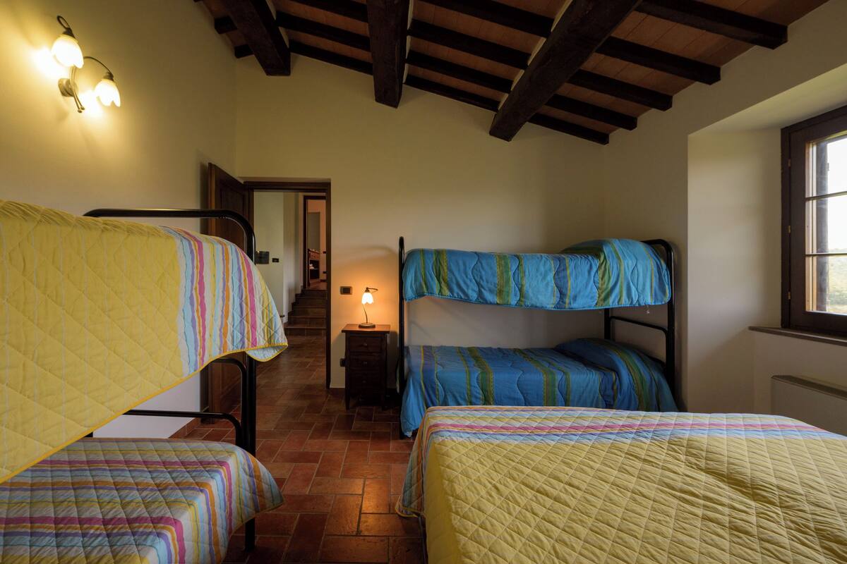 Un dormitorio con literas, una escalera y una mesita de noche con lámpara.