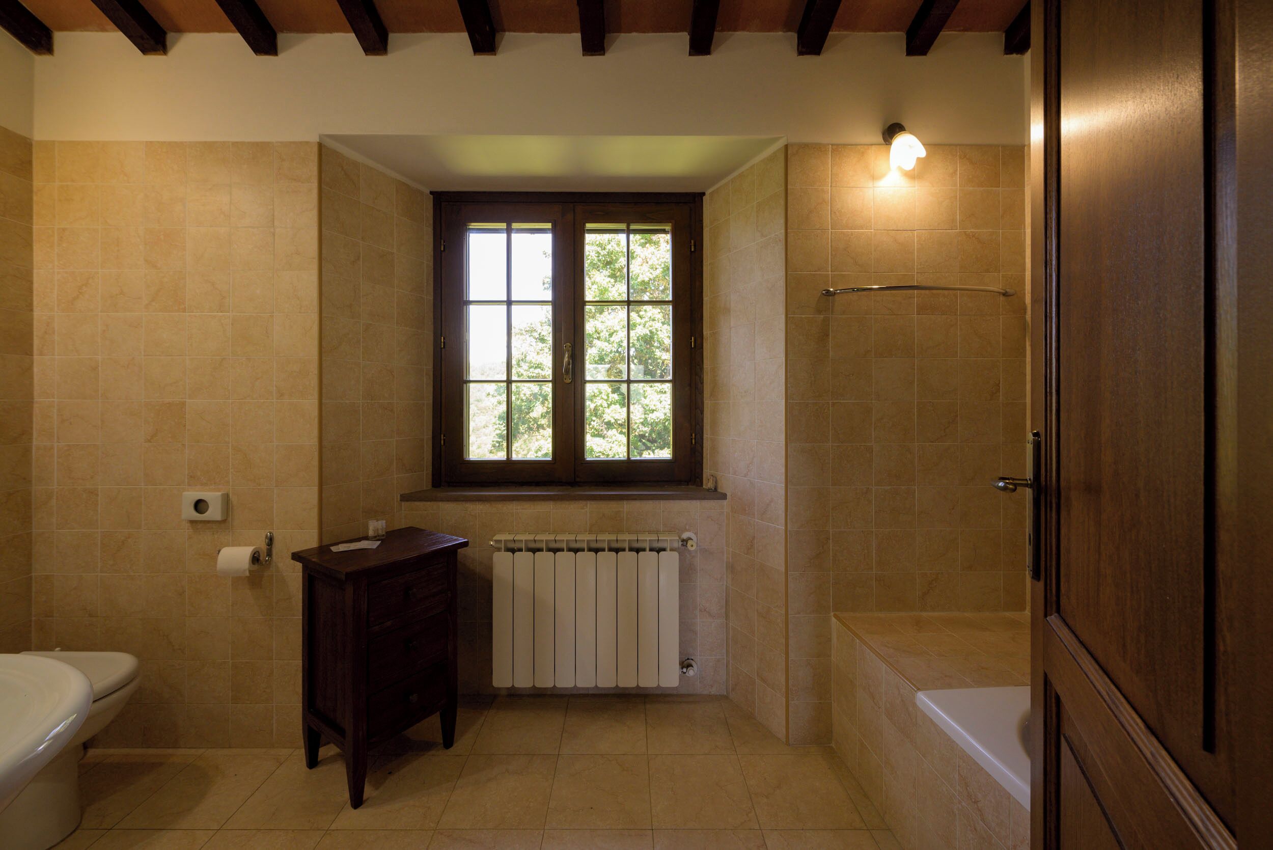 A bathroom with a toilet, a sink, a window, a shower, and a radiator.