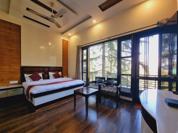 A modern bedroom with a large bed, a desk, and a balcony with a view of trees.