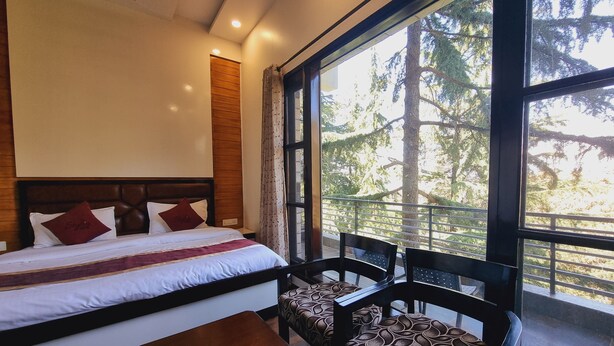 A bedroom with a large window, a bed with pillows, a wooden headboard, and a bench with patterned upholstery. - Stylia Suites (Dalhousie)