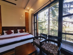 A bedroom with a large window, a bed with pillows, a wooden headboard, and a bench with patterned upholstery.