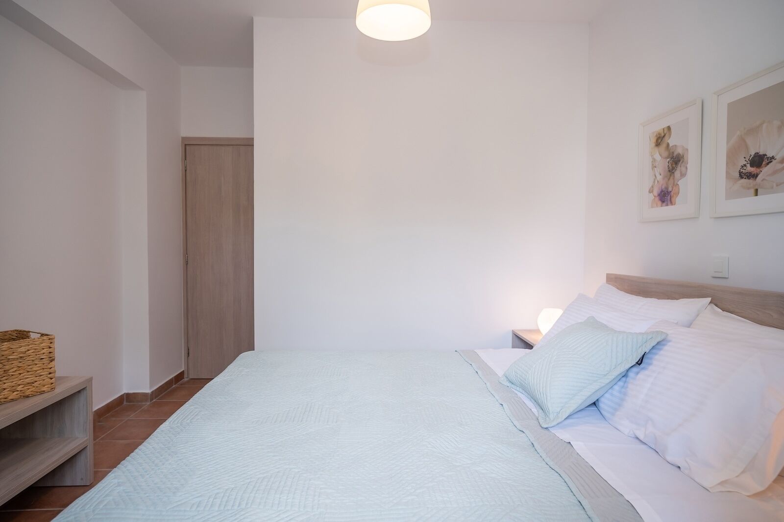 Ein Schlafzimmer mit Bett, Nachttischen, einer Lampe, einer Holztür und einem an der Wand befestigten Regal.